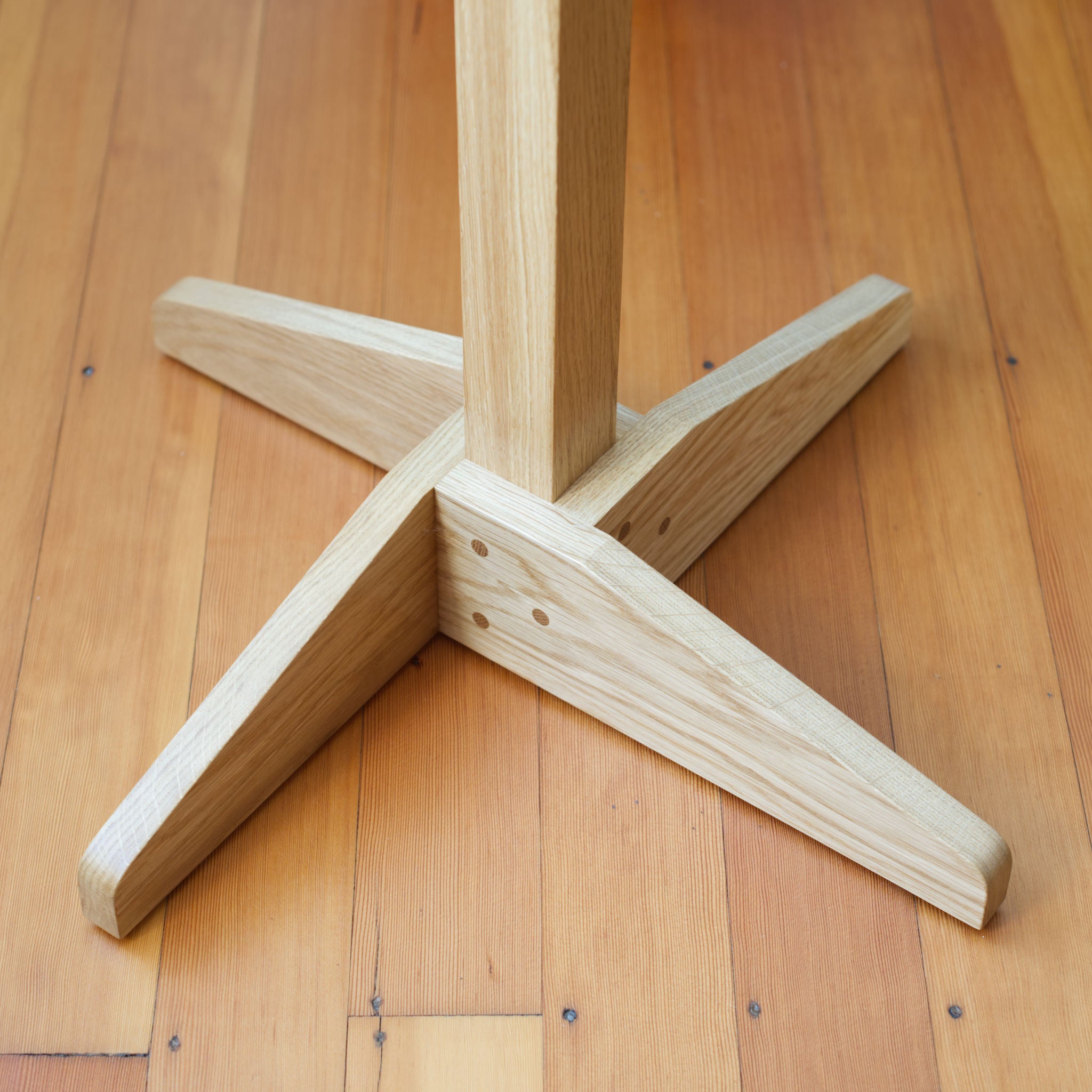 Wooden oak coat tree coat stand base on a wooden floor.