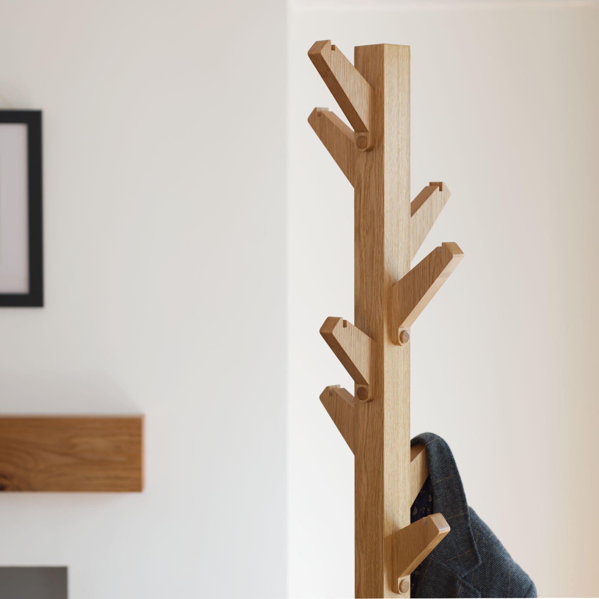 Wooden oak coat tree coat stand with multiple hooks against a white wall.